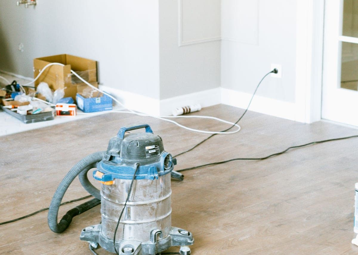 Aspirateur de chantier et balai large sur le sol d'une pièce en fin de travaux